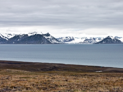 Panorama van besneeuwde bergen aan de kust van Spitsbergen, met zee en toendra onder een bewolkte lucht.