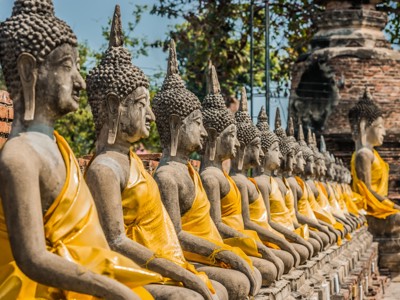 Rij boeddhabeelden met gele doeken bij tempelruïnes in Thailand tijdens de Route Thailand.