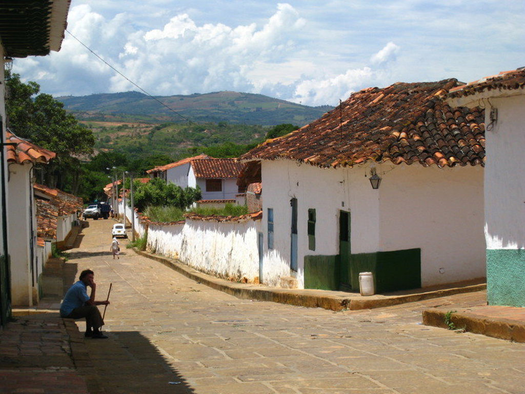 Straat in Colombiaans dorp met witte huizen en rode dakpannen, met groene heuvels op de achtergrond.