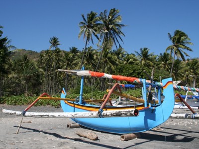 Traditionele vissersboot op het strand van Lombok, met palmbomen op de achtergrond.