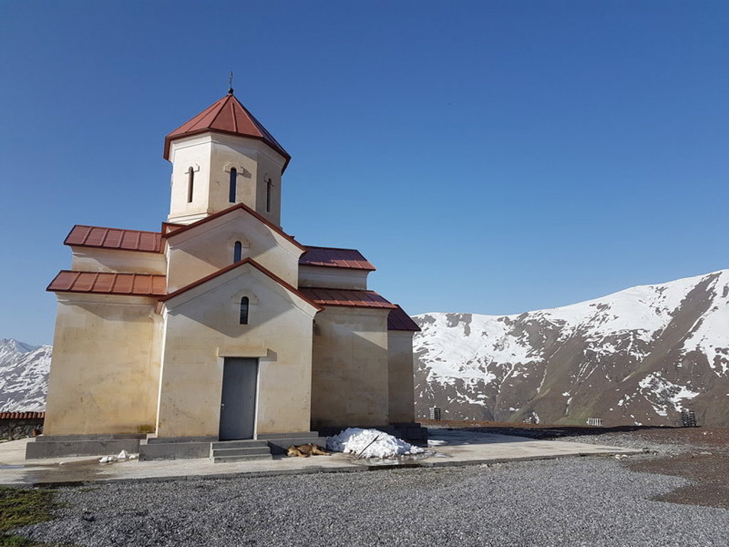 Gergeti Drievuldigheidskerk bij Kazbegi in Georgië, met besneeuwde bergen op de achtergrond.