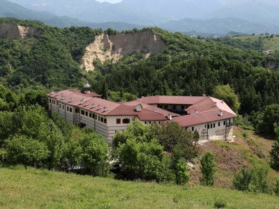 Kloostercomplex met rood dak in de Bulgaarse Balkan, omringd door groene heuvels en bergen.