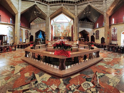 Interieur van de Kerk van de Aankondiging in Nazareth met altaar, muurschilderingen en mozaïekvloer.