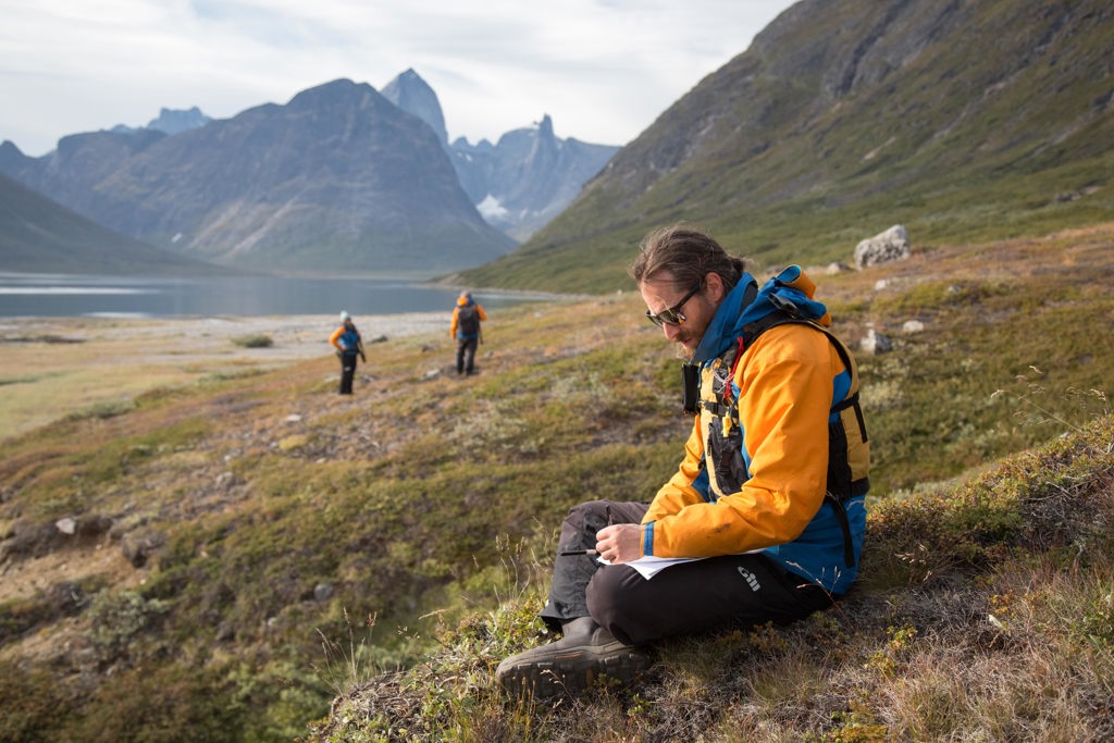 Wandelaar met kaart tijdens trekking in Groenland bij Disko Bay, met fjord en bergen op de achtergrond.