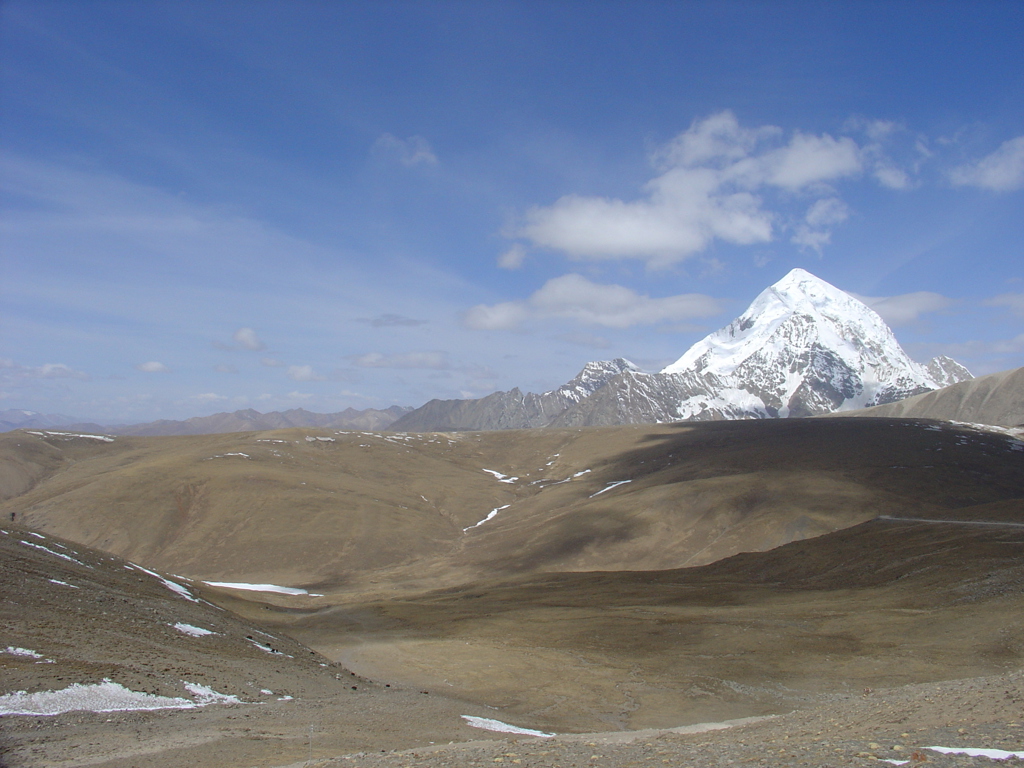 Sneeuwbedekte bergtop in Tibet met uitgestrekte hoogvlakte onder een blauwe lucht.