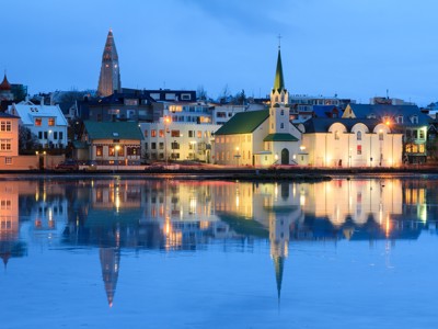 Avondzicht op Reykjavik met Hallgrímskirkja en kerk aan het water, weerspiegeld in een bevroren meer.