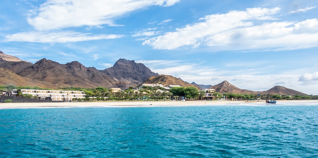 Zandstrand op Kaapverdië met turquoise zee, resorts en berglandschap op de achtergrond.