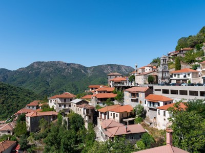 Bergdorp in Griekenland met stenen huizen en rode daken, uitzicht over groene bergen tijdens familiereis.