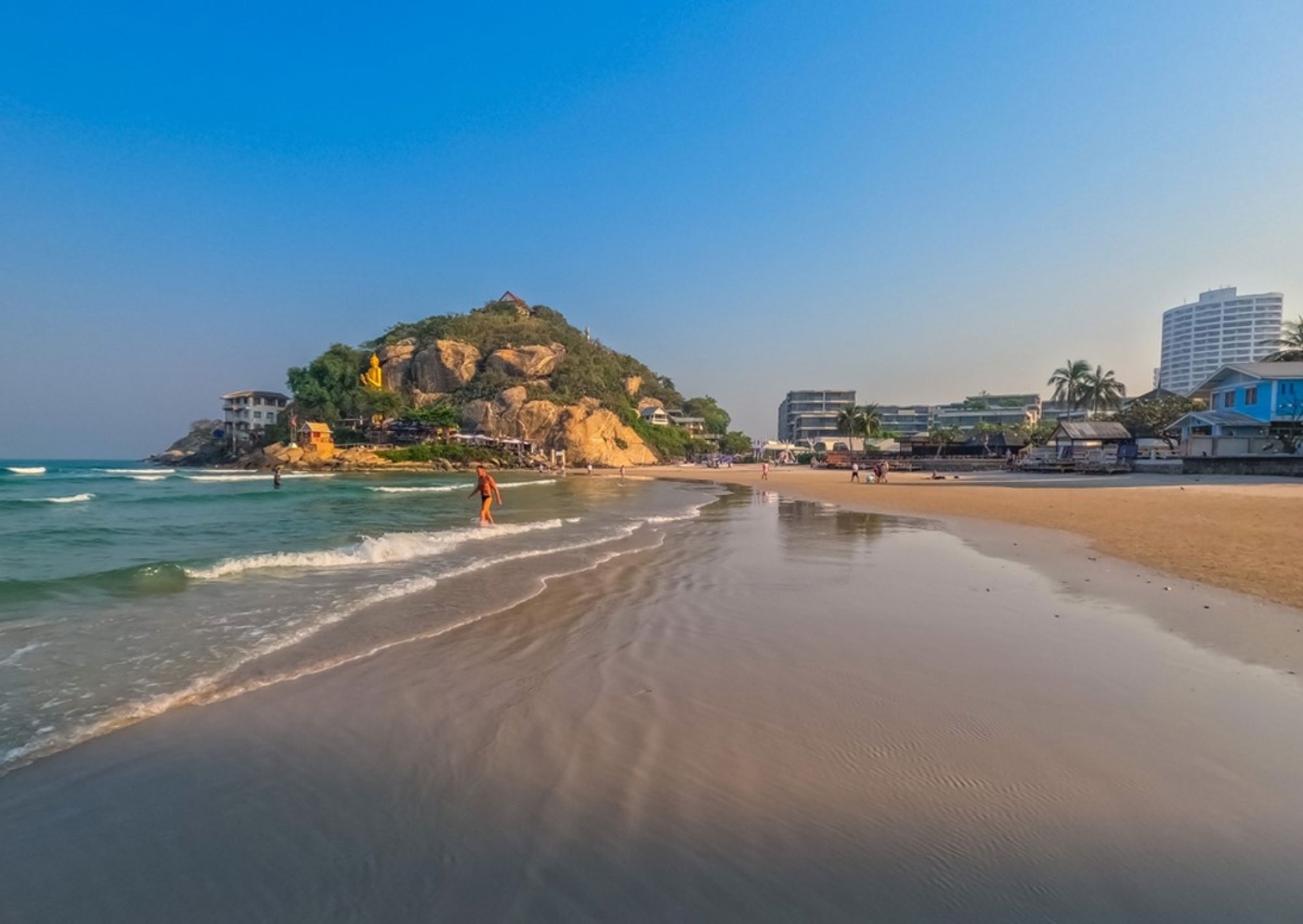 Zandstrand in Thailand met rotsheuvel, kalme zee en hotels langs de kustlijn.