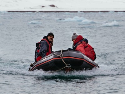 Zodiac met reizigers in rode jassen vaart tussen drijvend ijs tijdens de Spitsbergen-route.