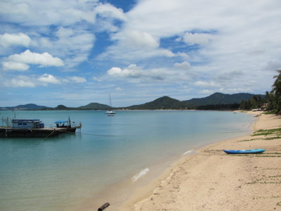 Rustig strand op Ko Samui met helderblauw water, een aanlegsteiger en zeilboot voor de kust.