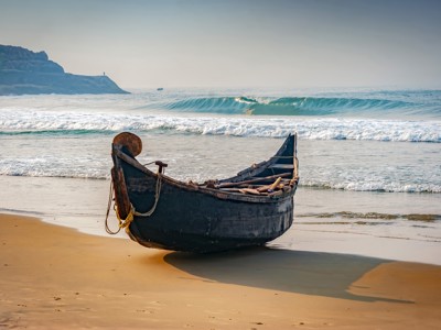 Houten vissersboot op het strand aan de kust van Zuid-India, met golven op de achtergrond.