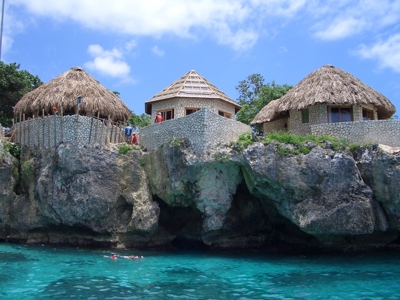 Rieten huisjes op kliffen boven helderblauw zeewater in Jamaica, route Jamaica 16 dagen.