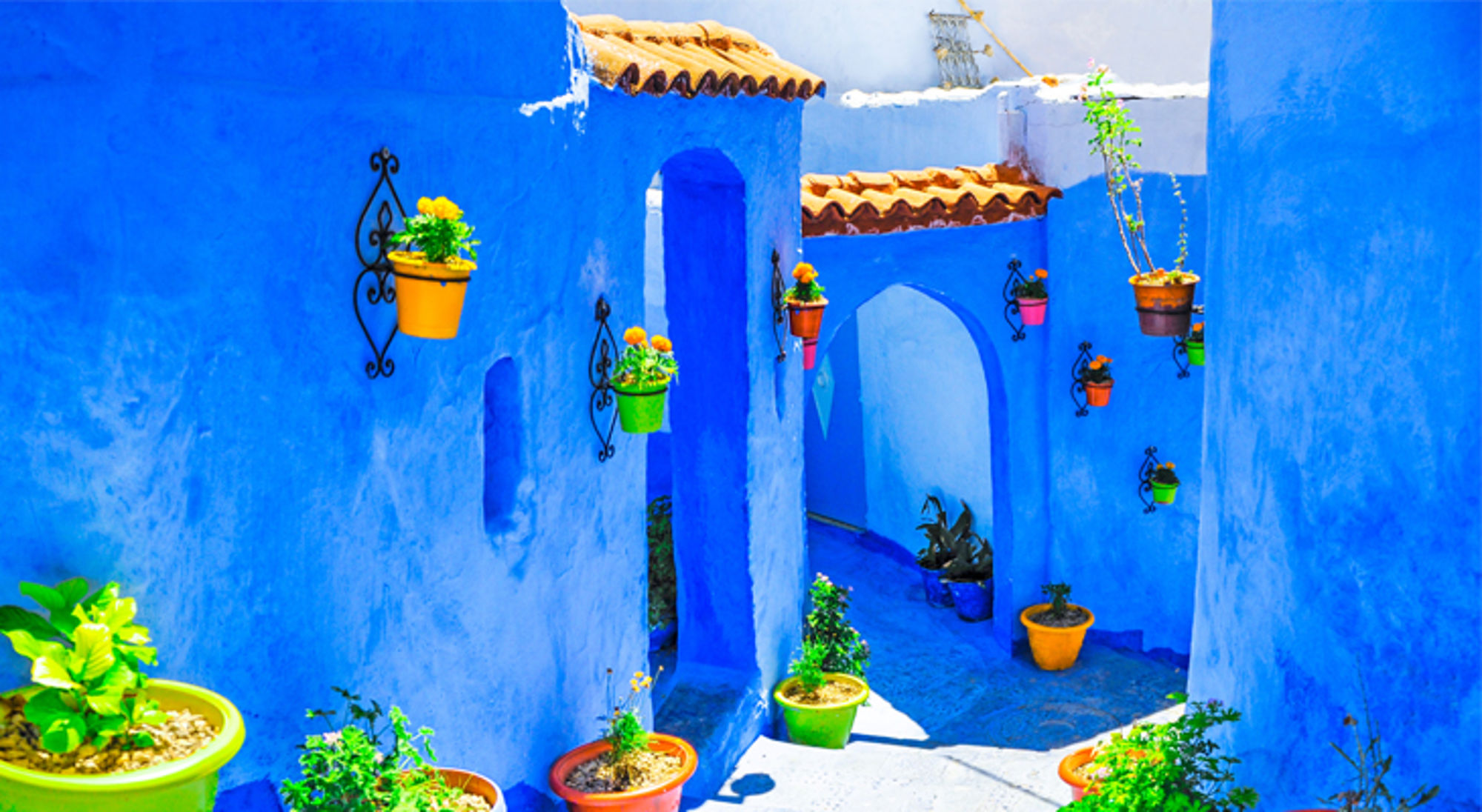 Blauwe steeg met bogen en kleurrijke bloempotten aan de muren in Chefchaouen, Marokko.