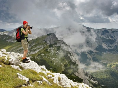 Wandelaar maakt foto op bergkam tijdens 10-daagse wandelvakantie in Bosnië & Herzegovina, met wolken en pieken.