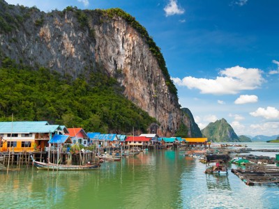 Kleurrijke vissershuisjes aan het water met longtailboten bij kalkstenen kliffen in Thailand.
