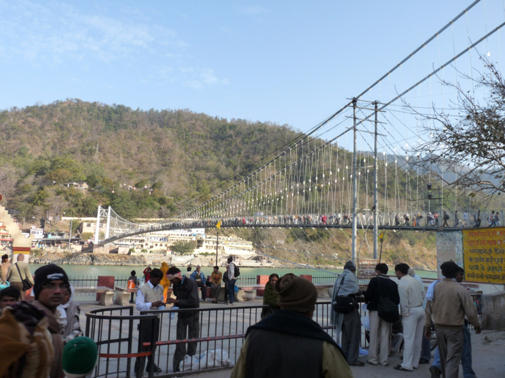 Hangbrug over de rivier in Rishikesh, India, met wandelaars en heuvels op de achtergrond.