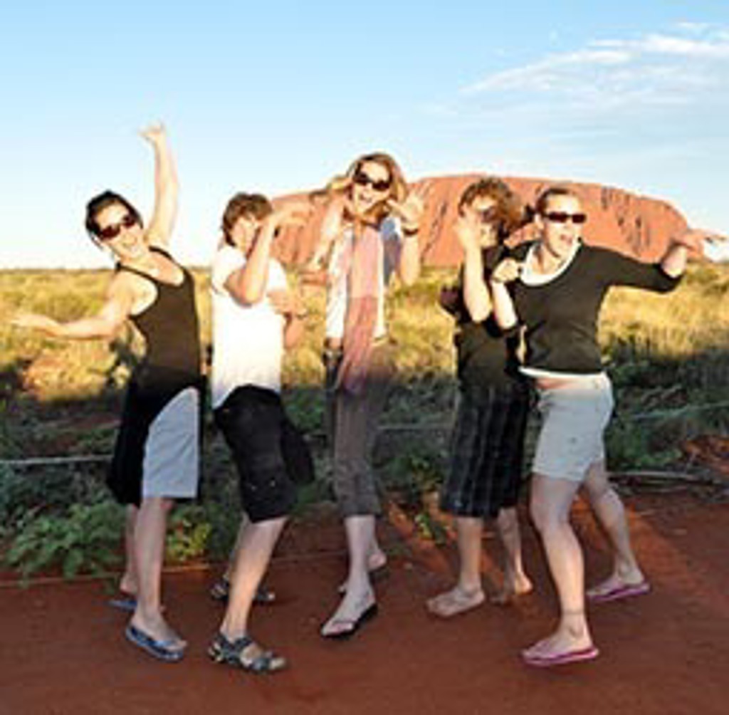 Vriendengroep poseert bij Uluru tijdens rondreis Australië met kamperen en hotels.