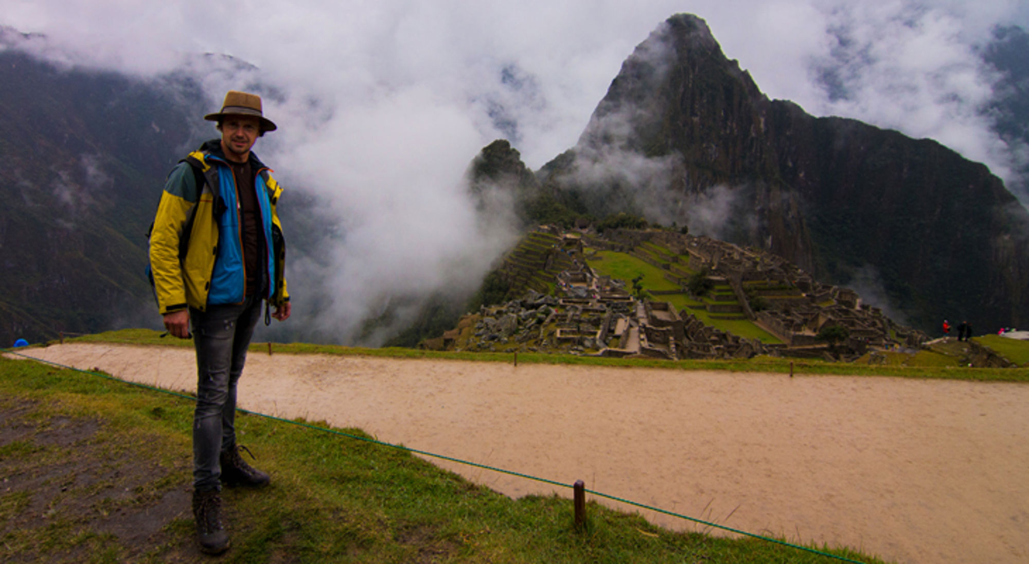 Bastiaan bij Machu Picchu in Peru Man poseert bij Machu Picchu met Huayna Picchu op de achtergrond, omringd door mist en bergen.