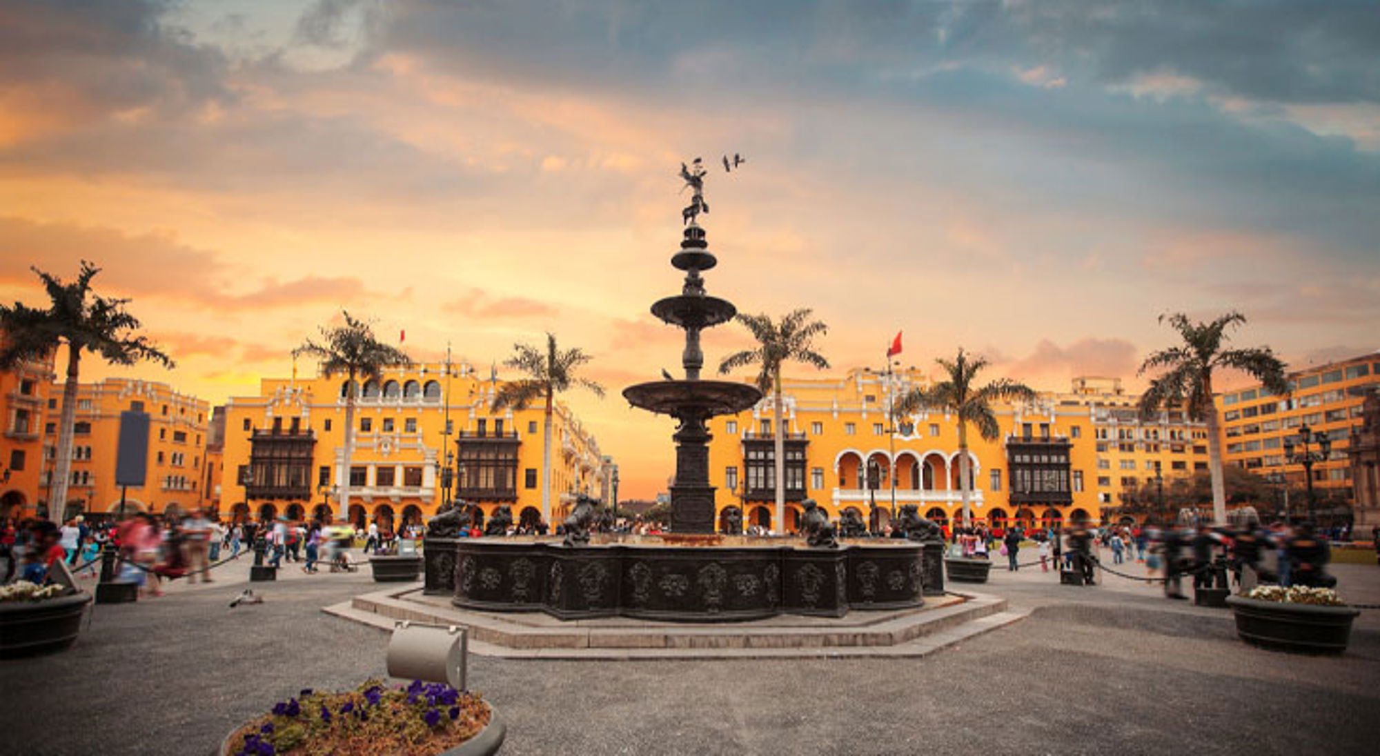 Fontein op Plaza Mayor in Lima, met gele gebouwen en palmbomen bij zonsondergang.
