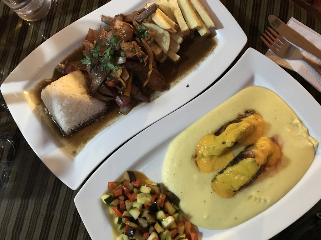 Peruaanse maaltijd met vlees in saus, rijst en friet, naast vis in romige saus en groentemix.