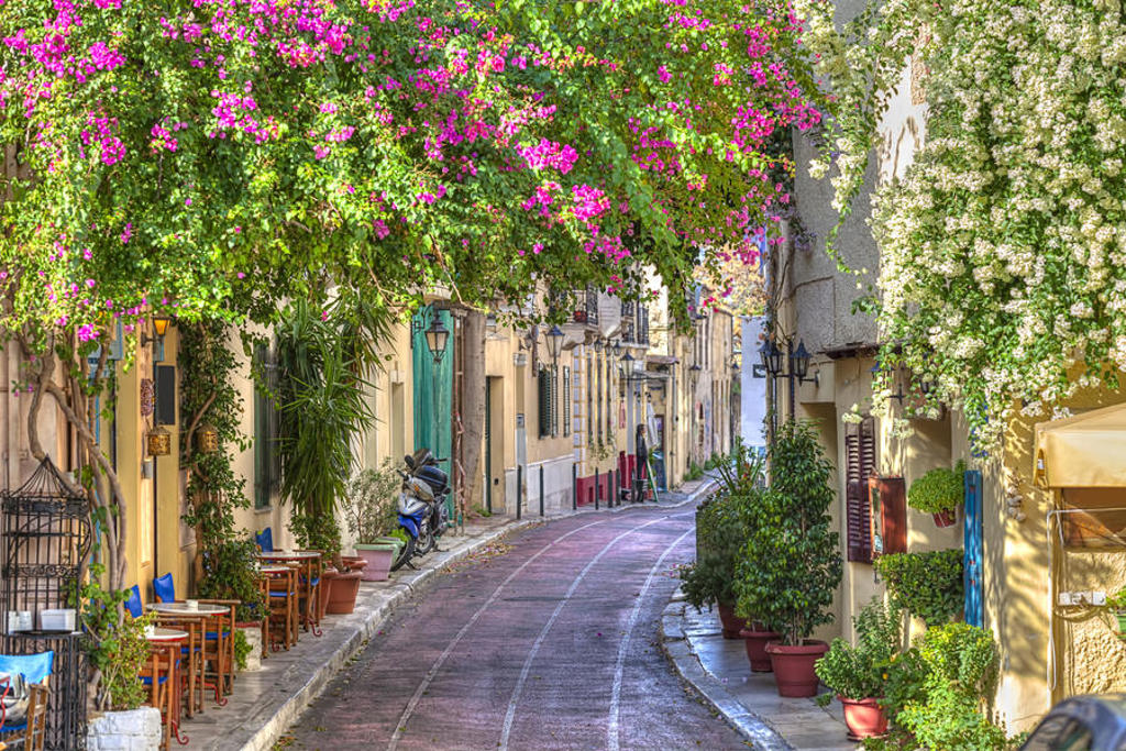 Sfeervolle straat in Griekenland met kleurrijke bougainvillea en terrasjes, ideaal voor een familiereis in de meivakantie.