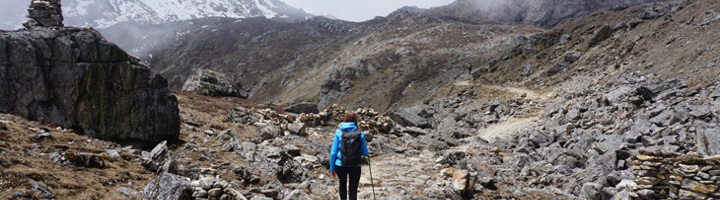 Wandelaar op bergpad tijdens de Annapurna-trek in de Nepalese Himalaya, met rotsen en besneeuwde toppen.