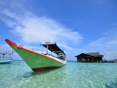 Kleurrijke boot in helderblauw zeewater bij een paalwoning op zee tijdens de route Bali & Sulawesi.