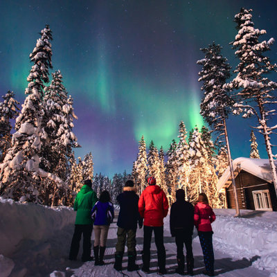 Reizigers kijken naar het noorderlicht boven een besneeuwd bos in Zweeds en Noors Lapland.