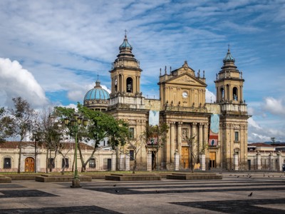 Kathedraal van Guatemala-Stad met klokkentorens en koepel aan een ruim plein onder een blauwe lucht.