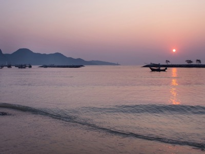 Zonsondergang bij het strand van Ko Samui met vissersboten op zee en bergen op de achtergrond.