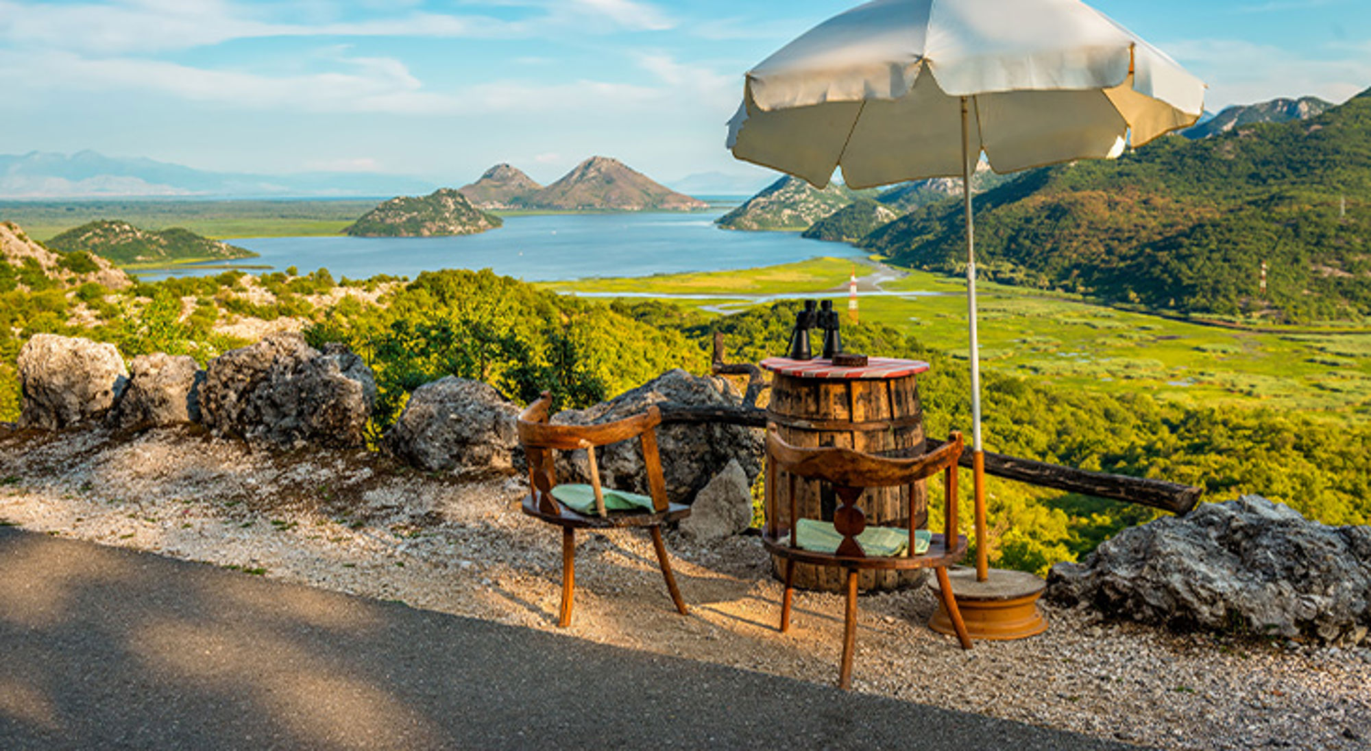 Montenegro Uitzichtpunt met stoelen en parasol met panoramisch uitzicht over een meer en bergen.