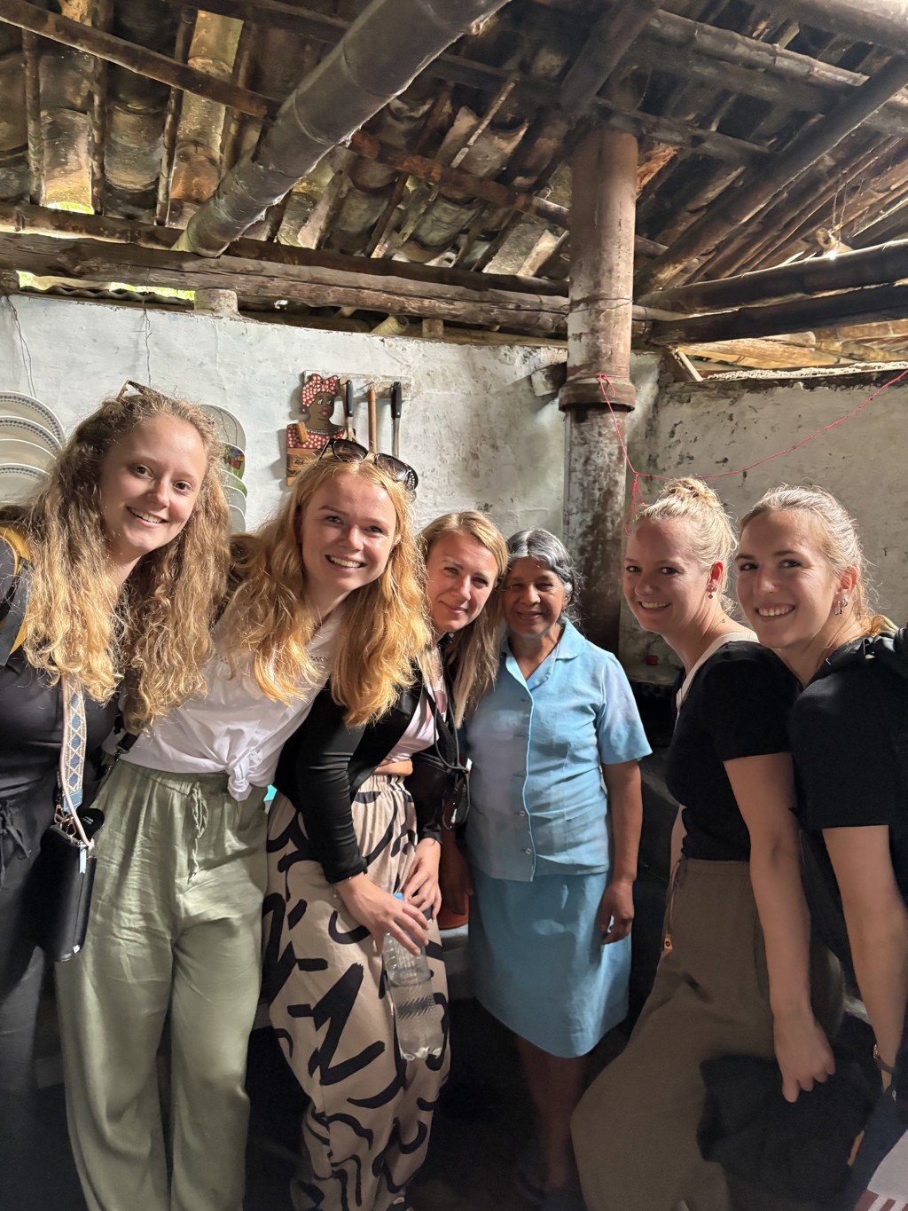 Groepsfoto van 22-35ers tijdens een rondreis door Colombia, samen met een lokale vrouw in een keuken.