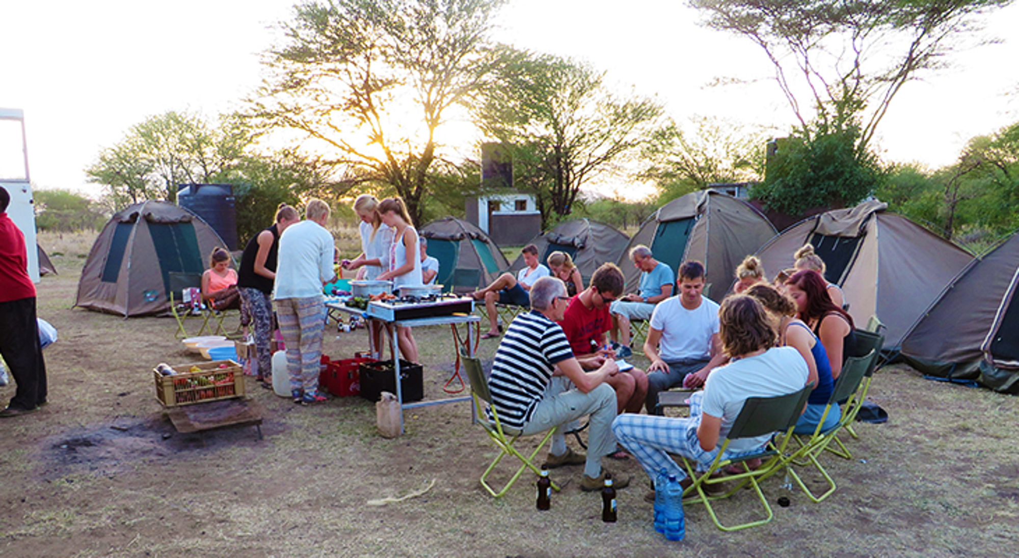 Kampeerders koken en eten samen op een safari-camping met tenten bij zonsondergang.