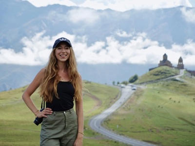 Reiziger bij de Gergeti Drievuldigheidskerk in Kazbegi, met berglandschap op de achtergrond.