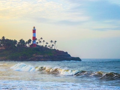 Rood-witte vuurtoren op rotsige kust met palmbomen en golven langs de Route Zuid-India.