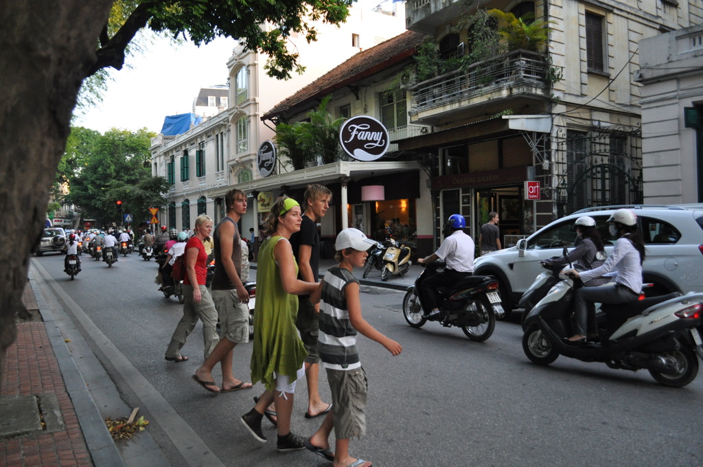 Gezin steekt een drukke straat met scooters over in Hanoi tijdens de Familiereis Vietnam Kort.