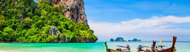 Longtailboten op het strand bij Koh Phi Phi, met turquoise zee en kalksteenklif op de achtergrond.