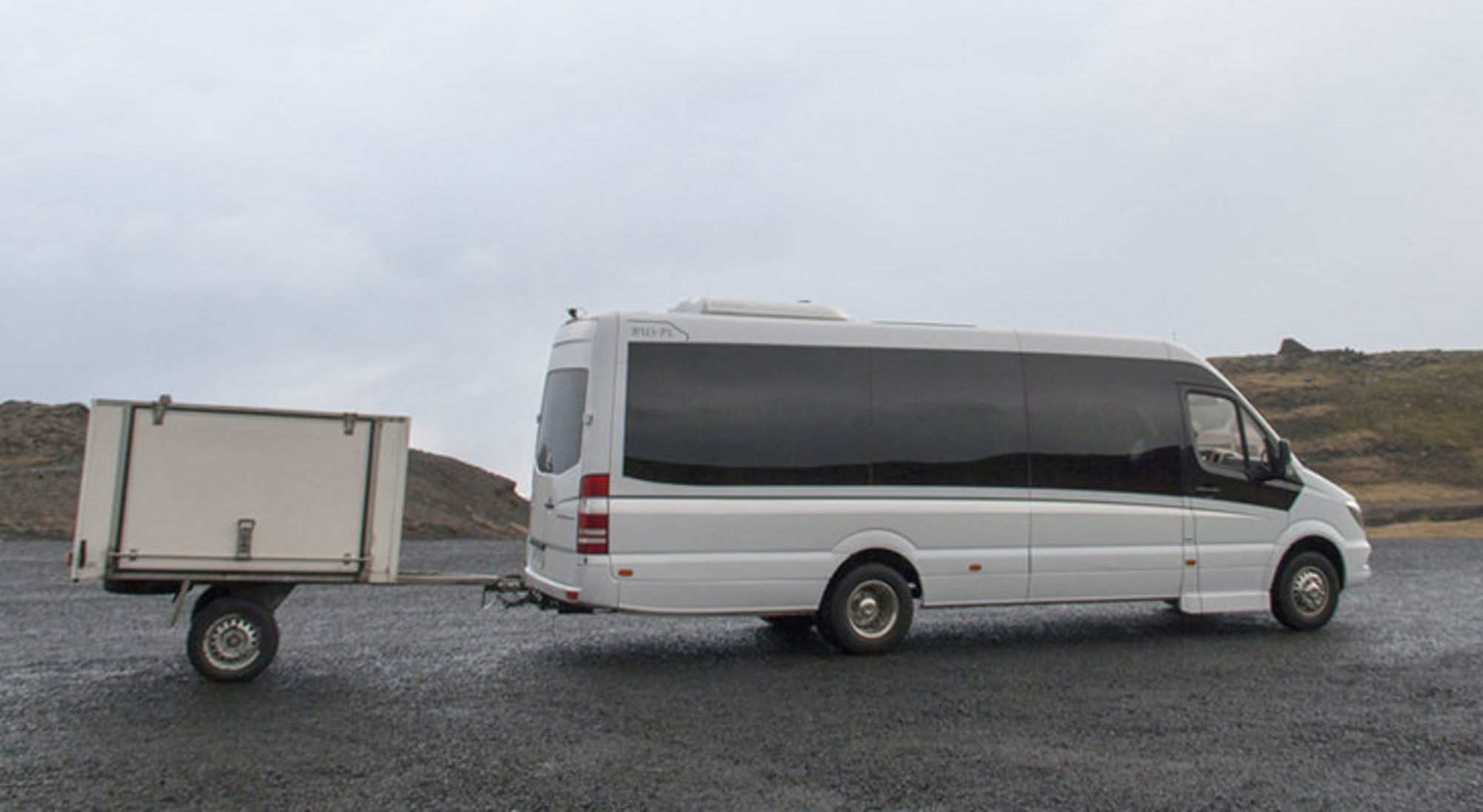 Witte minibus met aanhanger op een lege weg in IJsland.