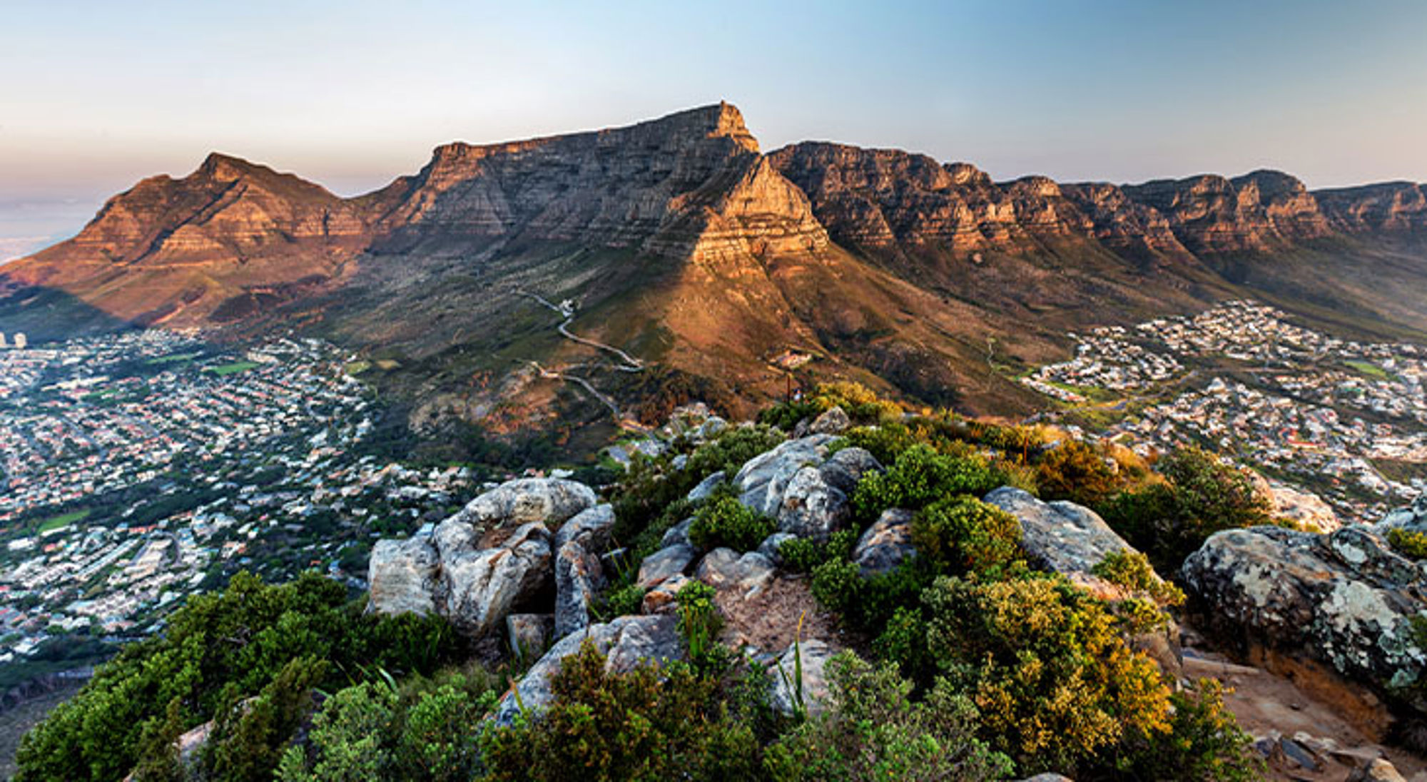 Tafelberg Kaapstad Zuid-Afrika Uitzicht op de Tafelberg bij Kaapstad tijdens zonsondergang, met rotsen en groen op de voorgrond.