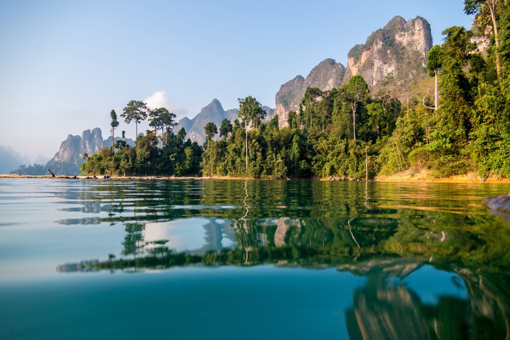 Kalkstenen rotsen en groen oerwoud langs een rustig meer in Thailand, met spiegeling in het water.
