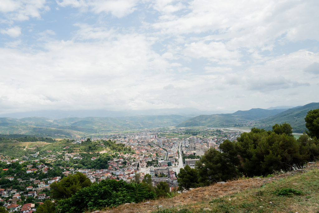 Panoramisch uitzicht over een stad in Albanië, omringd door groene heuvels en bergen.