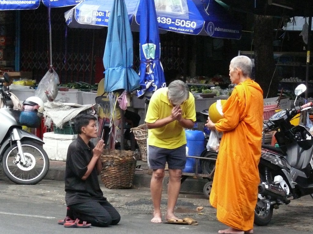 Thaise monnik ontvangt aalmoes op straat, terwijl twee mensen biddend knielen tijdens rondreis Thailand Noord en Zuid.