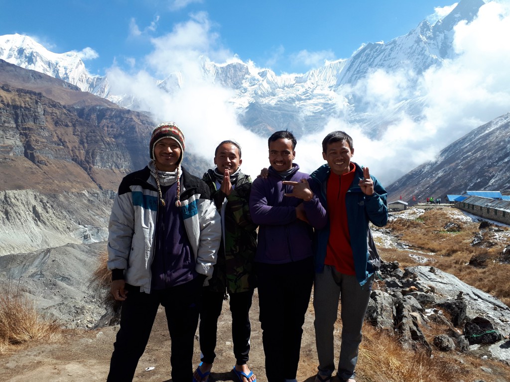 Dragers en gidsen poseren bij Annapurna Basecamp met besneeuwde Himalayapieken op de achtergrond.