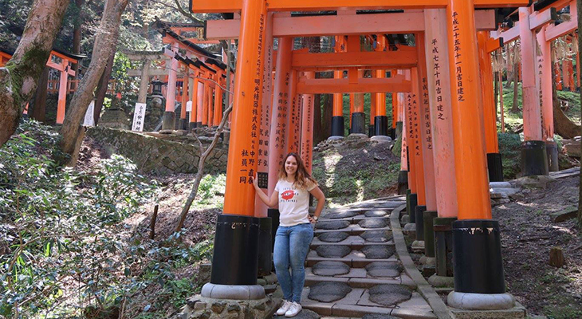 Deborah Vrouw poseert tussen de oranje torii-poorten van Fushimi Inari-taisha in Kyoto, Japan.