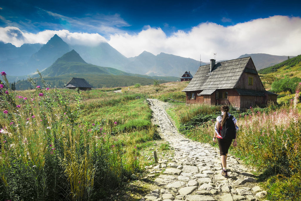 Wandelaar op bergpad langs houten berghutten met uitzicht op de Hoge Tatra, Centraal-Europa.