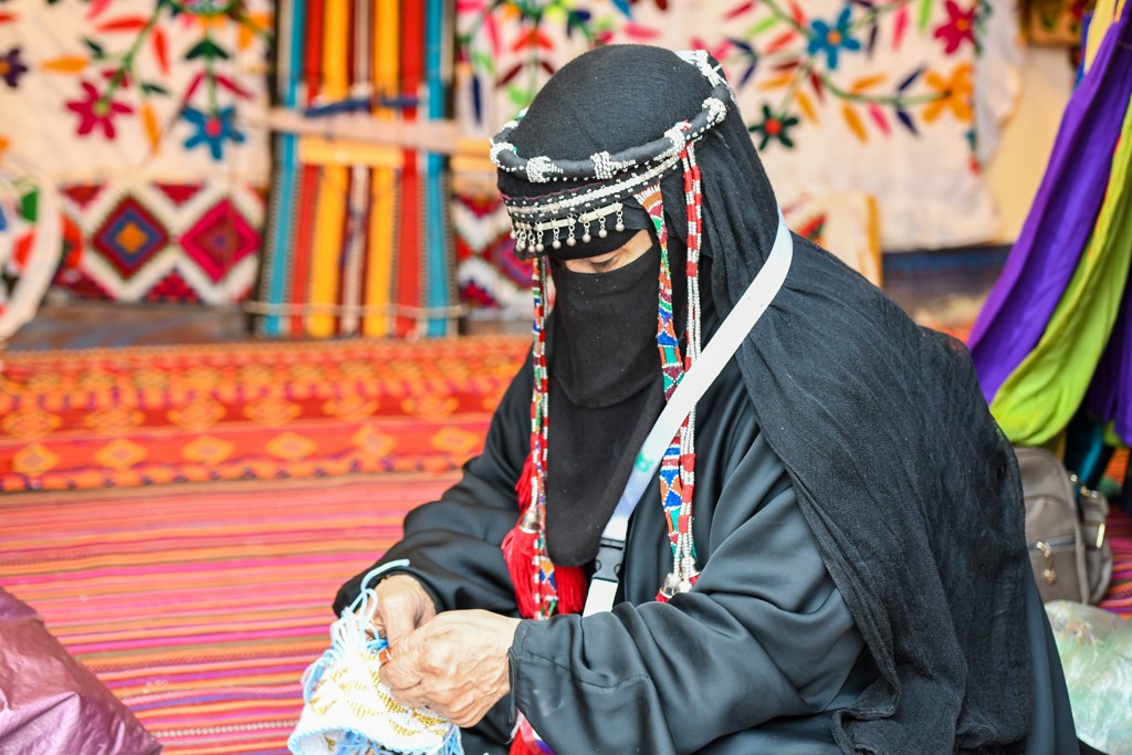 Vrouw in traditionele kleding maakt handwerk in een kleurrijke tent tijdens groepsrondreis door Saoedi-Arabië.