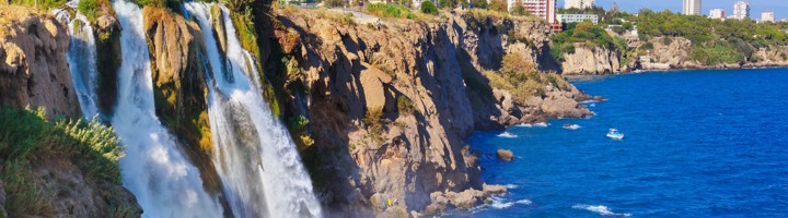 Düden Waterfalls bij Antalya: waterval stort van de kliffen in zee, met skyline op de achtergrond.