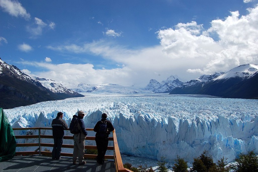Uitzicht op de Perito Moreno-gletsjer in Patagonië vanaf een uitkijkplatform, met besneeuwde bergen op de achtergrond.