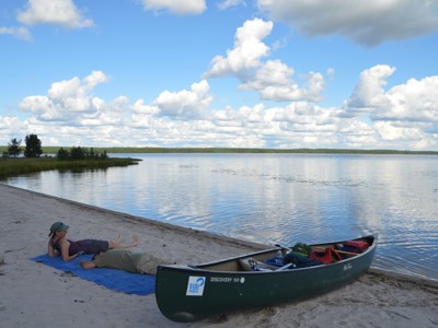 Kanotocht in Lapland: kano op het strand bij een rustig meer onder een blauwe lucht met wolken.